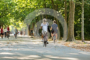 A young blond woman and man cyclingÂ in a sunny and green Amsterdam Vondelpark